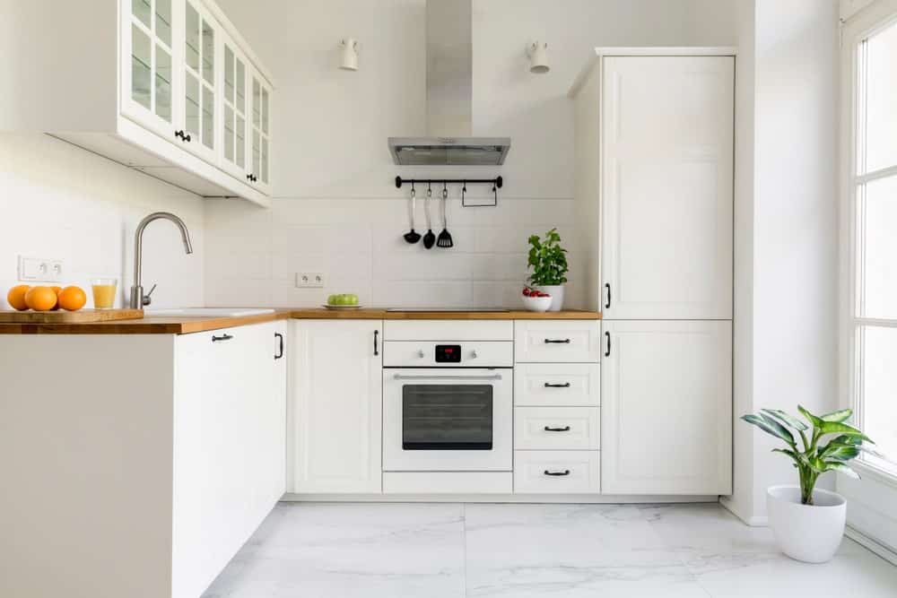 公寓厨房采用中性色调，展示白色橱柜，瓷砖后挡板，轻木台面，白色电器和大理石瓷砖地板。