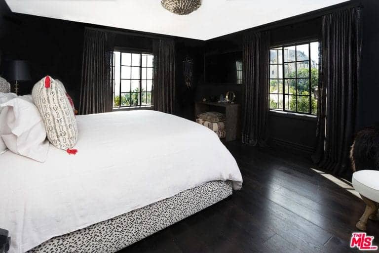 宽敞的黑白卧室有一面黑色的墙壁和深色的木墙，与白色的天花板和舒适的大床相匹配。