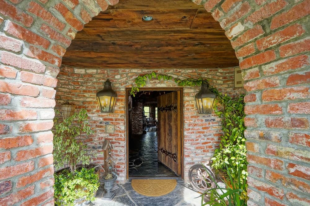 这座城堡般的豪宅的主入口由砖墙和装饰着盆栽和蔓藤的拱门以及两个迷人的壁挂式灯组成。图片来自Toptenrealestatedeals.com。