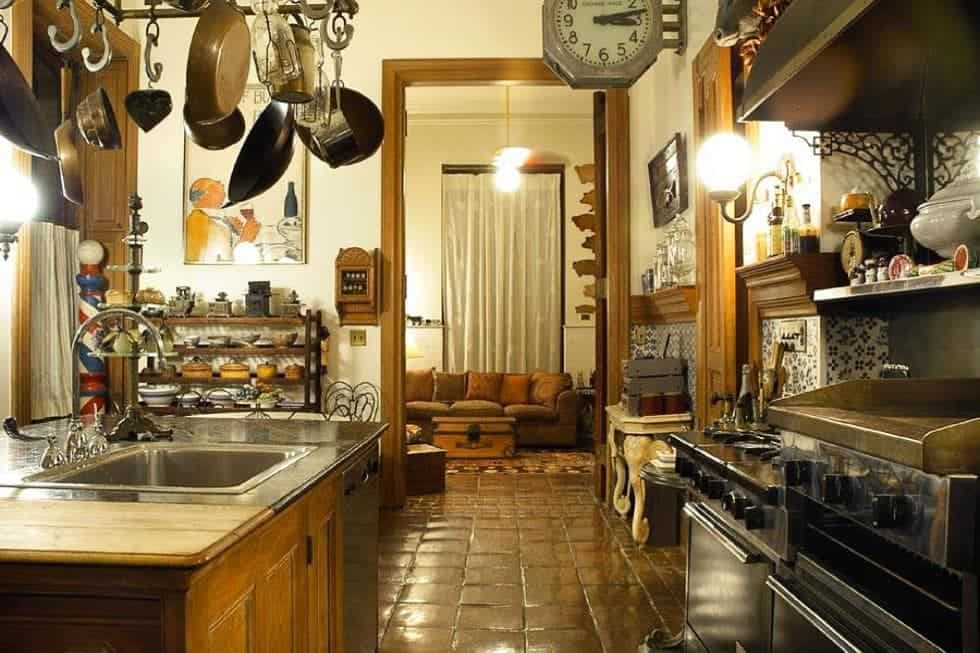 这是对厨房的近距离观察，在不锈钢烤箱对面的厨房岛上悬挂着锅碗瓢盆。这些都是由温暖的灯光和陶土地板补充。