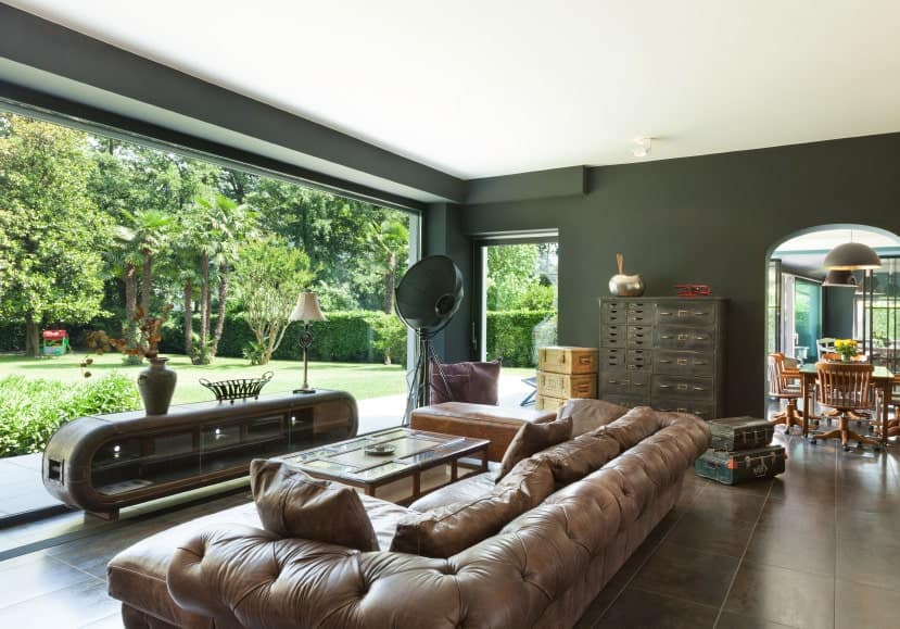 这个客厅的棕色皮革沙发套看起来很优雅。深绿色完成包围和全景窗户,房间是惊人的时尚和迷人的。