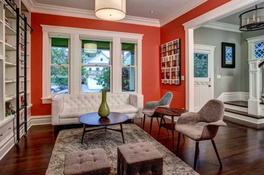 舒适的客厅以白色嵌壁式书架为特色，面向白色簇绒沙发和灰色座椅。一张圆形咖啡桌放在中间的蓬松地毯上。