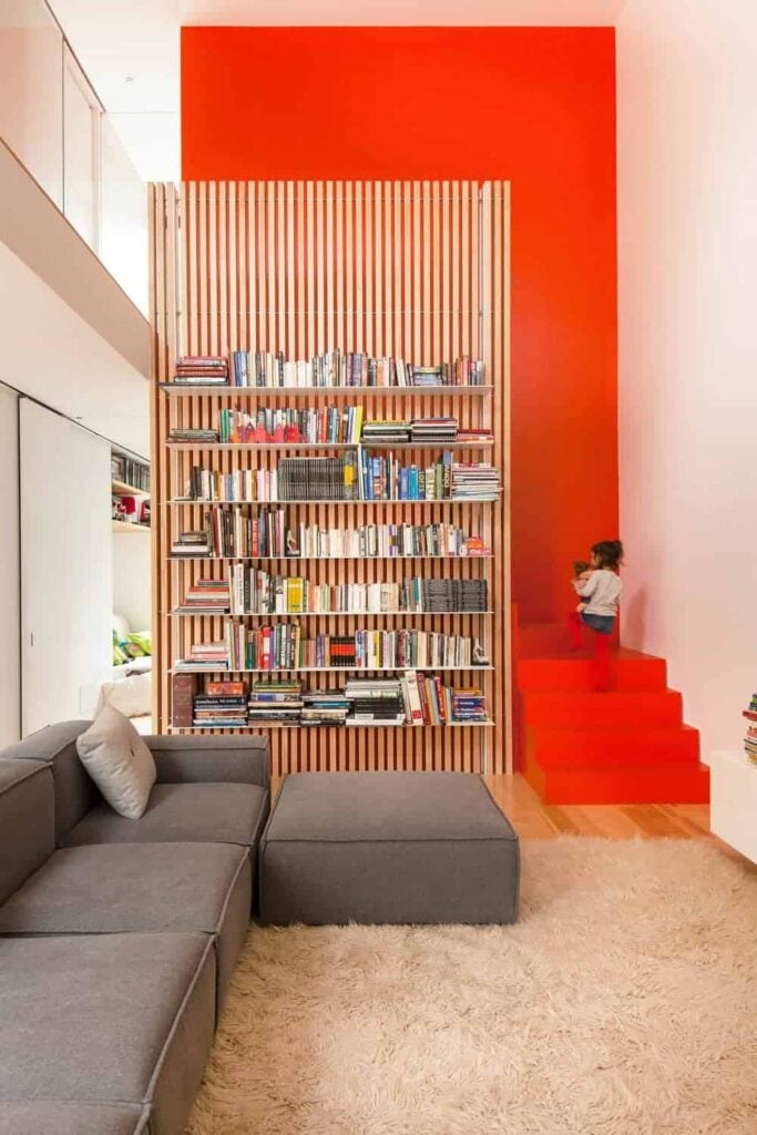 一个美丽的生活空间，以灰色沙发和蓬松的地毯为特色，以及多个内置书架。房间里有一个充满活力的橙色梯子，延伸到墙壁上。