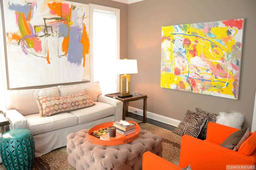 这个客厅展示了一个白色的裙边沙发和一对橙色的扶手椅，两侧是一个簇绒软凳。大型抽象画在灰色墙壁的映衬下格外显眼。