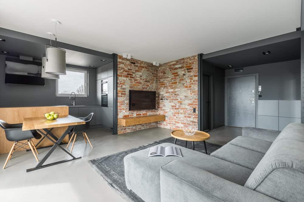工业风格的房间，漂亮的红砖墙和金属灰色色调与l型沙发相搭配。
