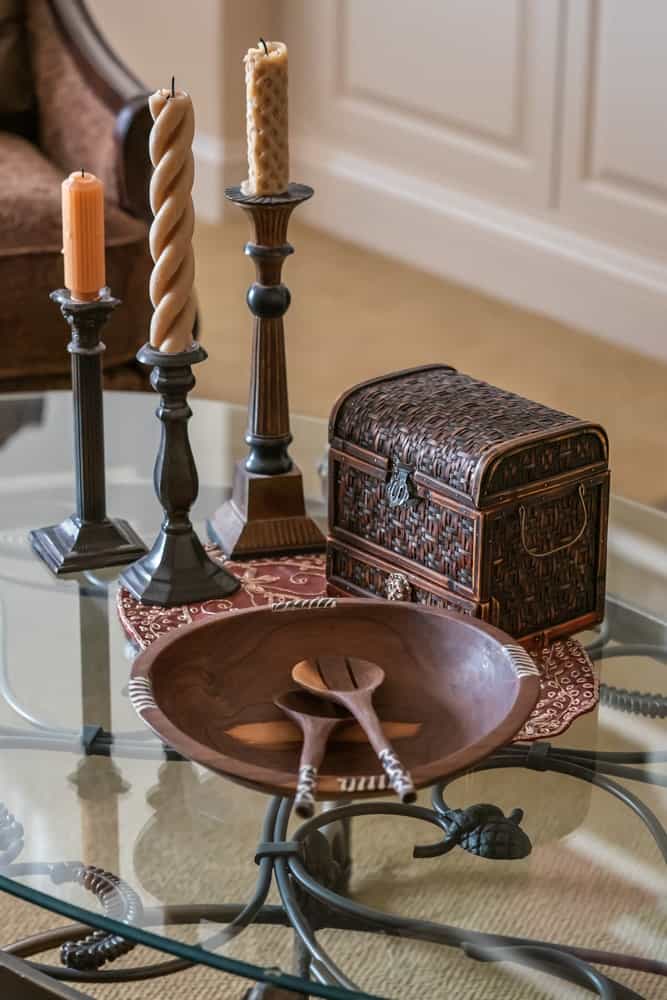 一张装饰着烛台的玻璃咖啡桌，一个木制的柜子和一个木制的盘子。