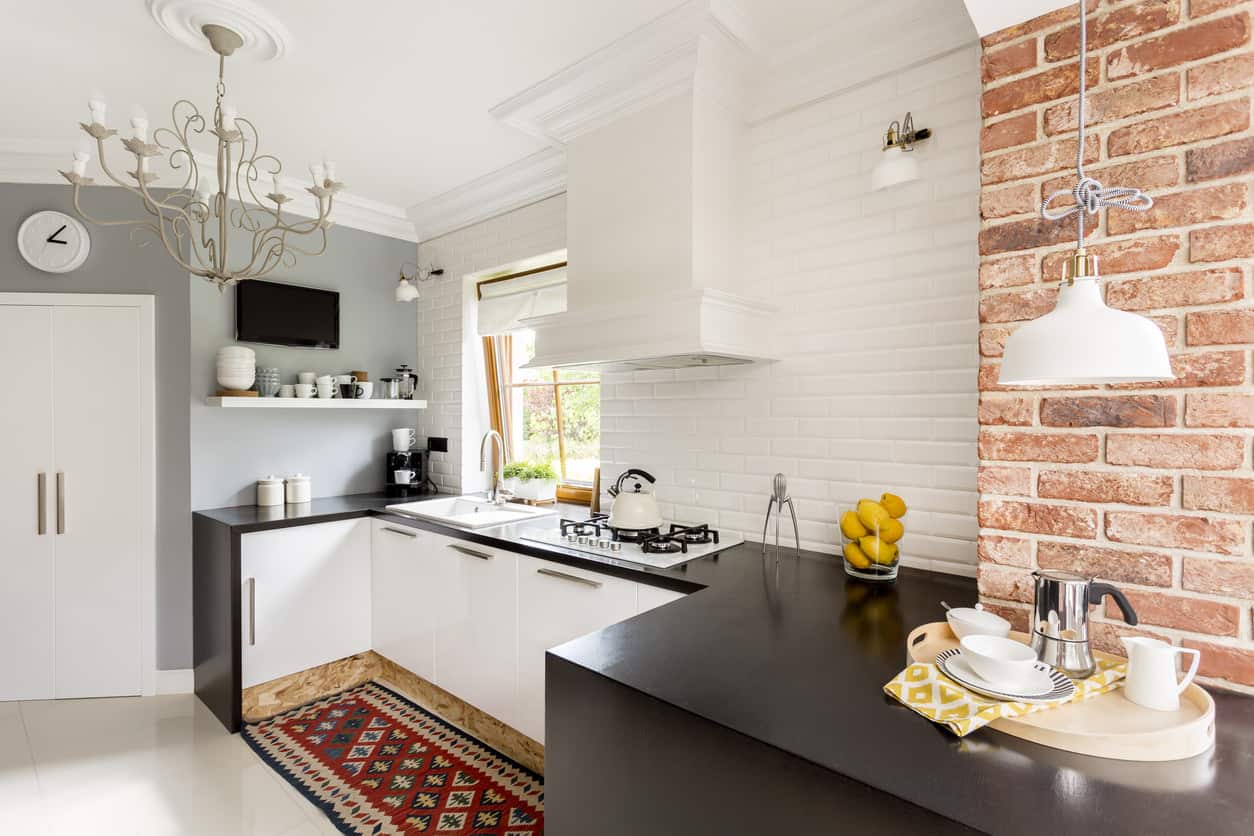 耀眼的白色和一个黑色的小厨房，白色的隔板靠近砖墙。黑色的台面与白色的整理面形成了和谐的平衡。