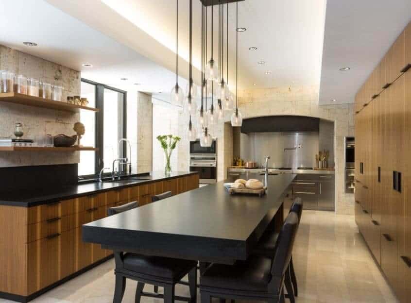 长而长方形的厨房岛台配有黑色台面，优雅的吊灯使其更加明亮。