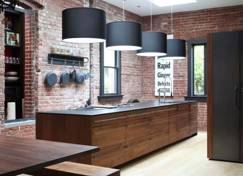 这间厨房有一个黑色台面岛台和一面砖墙。还有木质橱柜和木质餐桌。