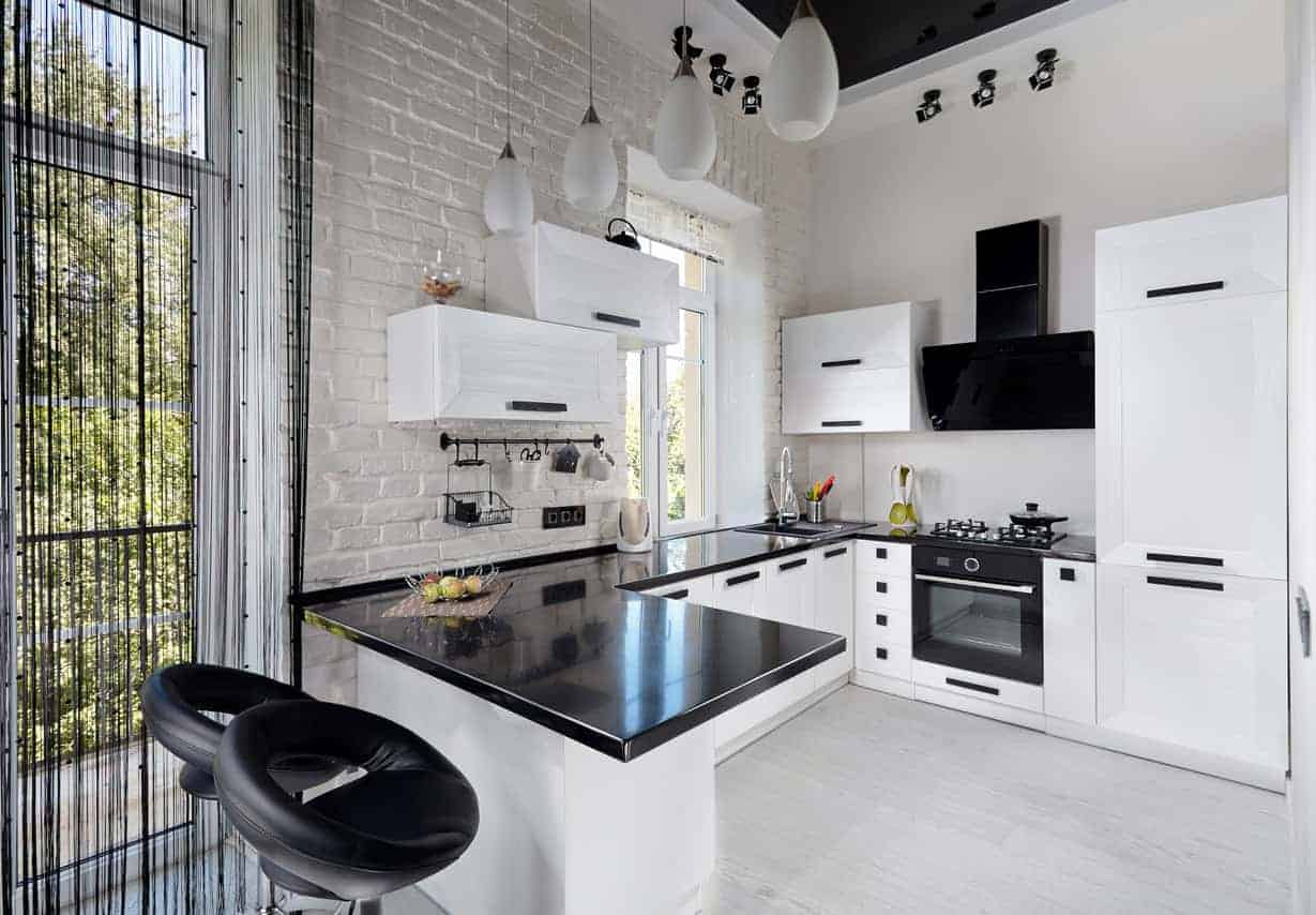 这间现代的黑白厨房有一个黑色台面和白色橱柜，与瓷砖地板相匹配。