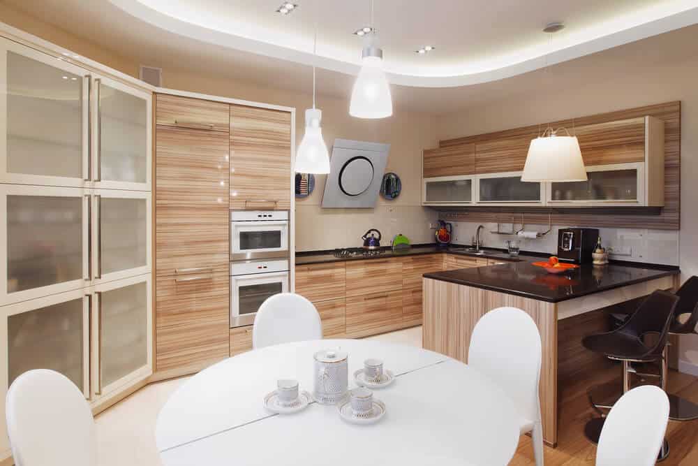 这个厨房与用餐区共用，白色餐桌和白色椅子。厨房以黑色台面和木制橱柜为特色。