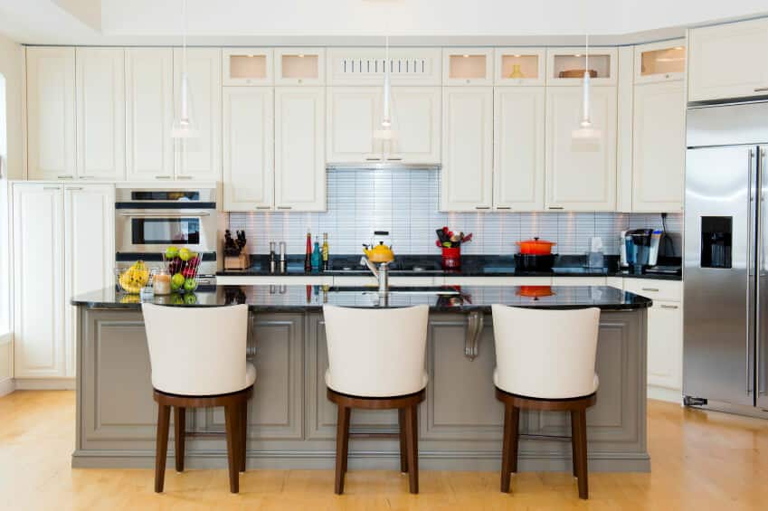 带浅灰色岛台的厨房配有餐厅座椅，设有黑色台面和完整的厨房水槽和白色橱柜。