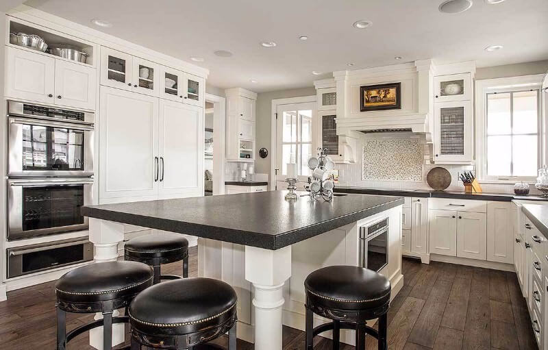 这个白色厨房的特色是深色台面和深色岛面。深色的地板和黑色的圆形凳子装饰继续形成深色的对比。