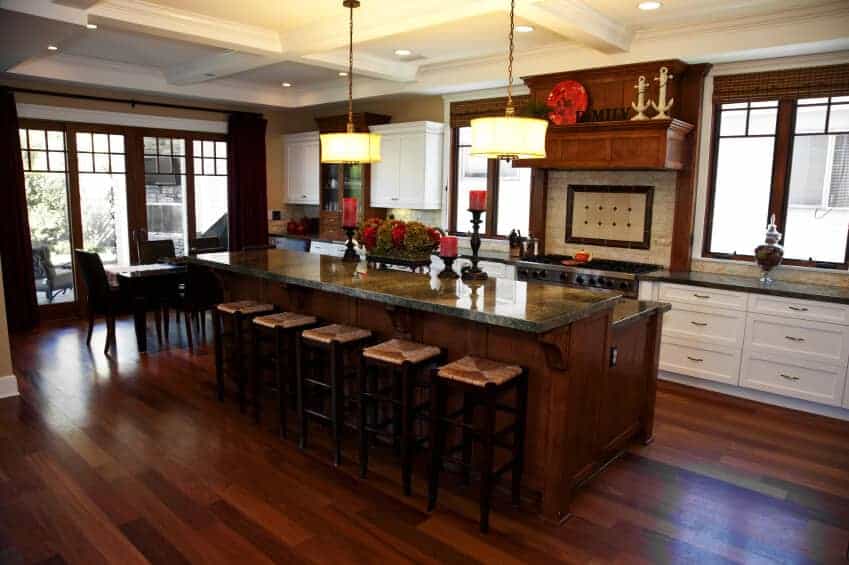 丰富昏暗的木材色调贯穿整个厨房，包括一个两层的岛，酒吧座椅和黑色大理石台面。