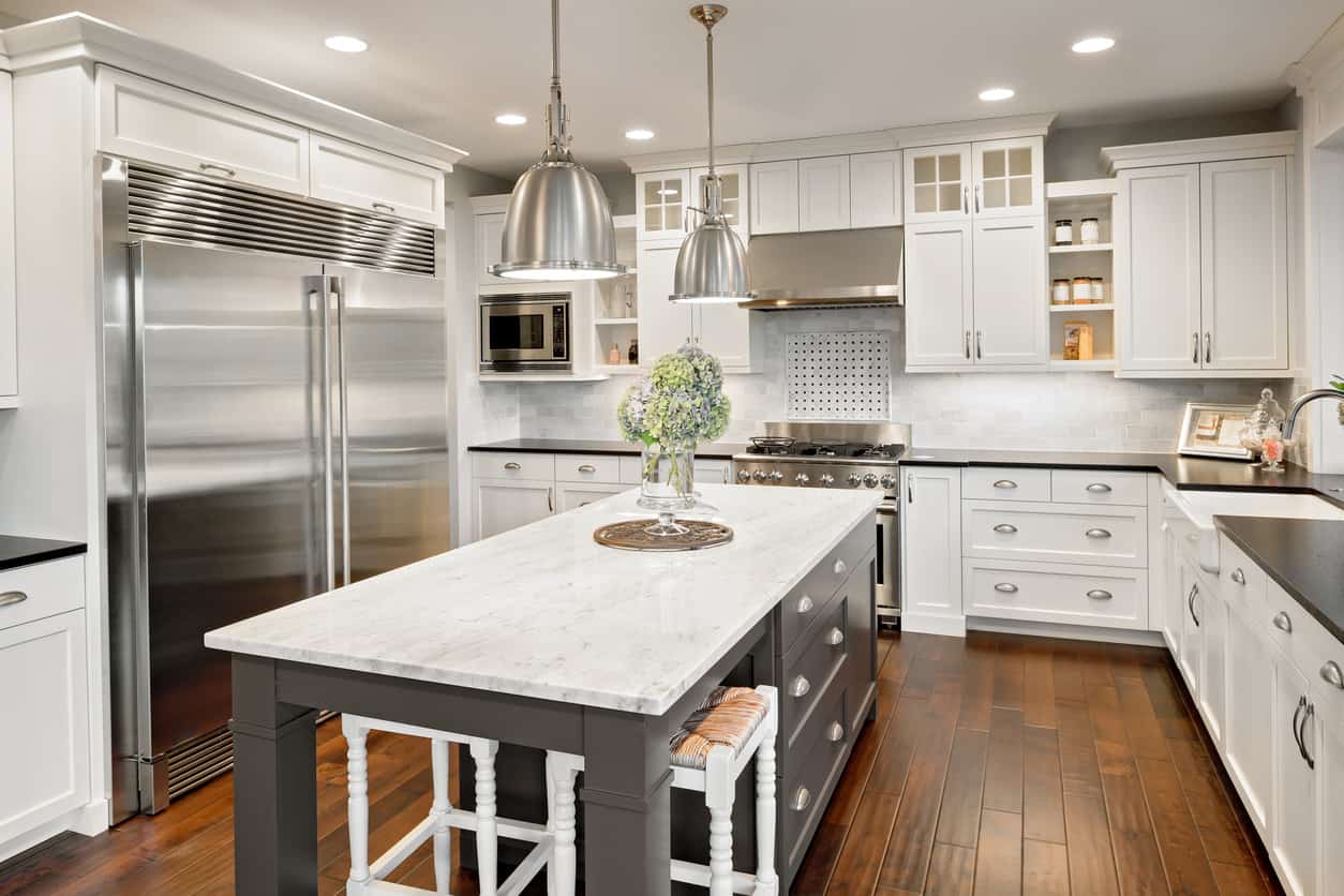 白色厨房的特色是白色橱柜和深色台面，并置带有白色表面的深灰色岛台
