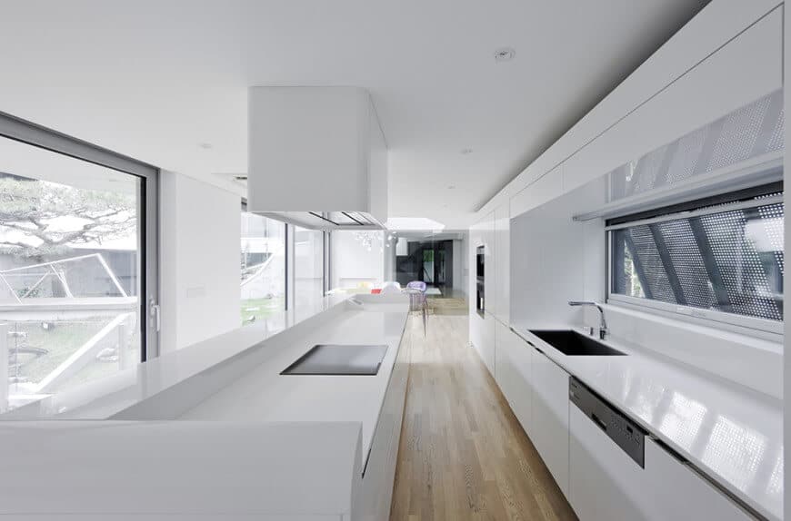 这个狭长的厨房设计有一个白色的台面，与白色的墙壁和天花板相匹配，天花板上有嵌入式灯。