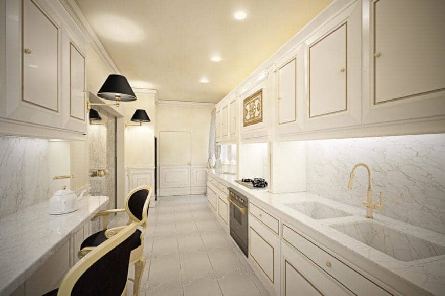 这个狭长的厨房里有白色的橱柜和抽屉，这些橱柜和抽屉都用精美的部件切割而成，与现代水槽上方的金色水龙头相匹配。