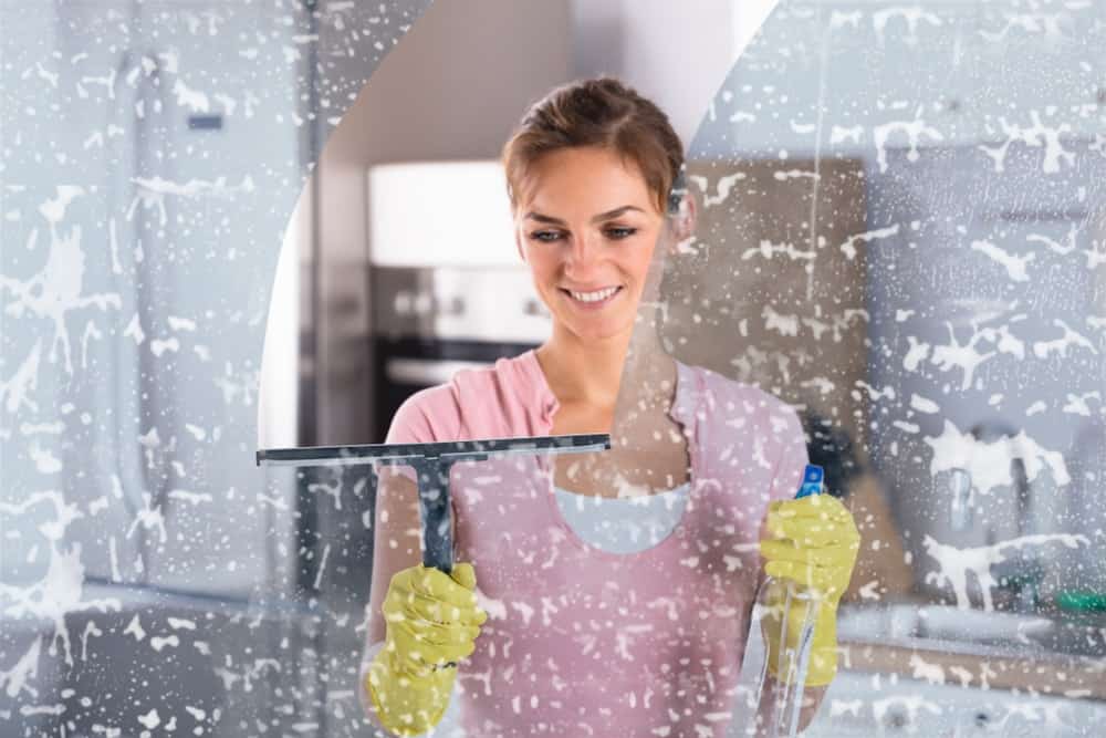 一名妇女正在用橡皮刷和喷雾器清洁窗户。