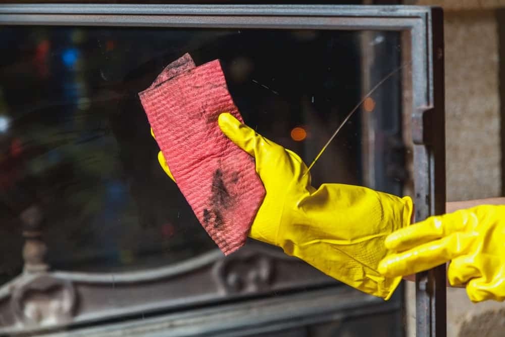 戴着手套的手用抹布擦拭干净透明的壁炉玻璃。
