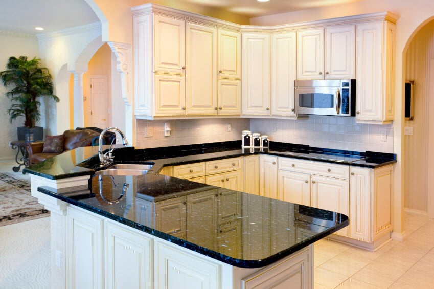 这间厨房提供厨房柜台，配有优雅的黑色花岗岩台面和米黄色橱柜，与瓷砖地板相匹配。