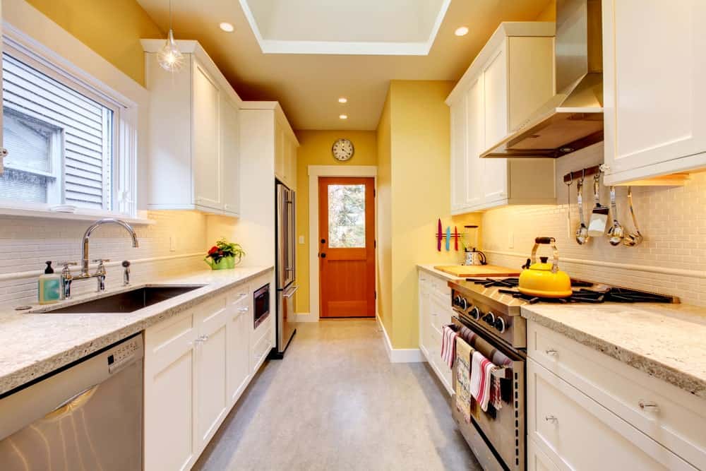 这间厨房设有不锈钢电器和白色橱柜，由灯泡吊坠和嵌入式天花板灯照明。