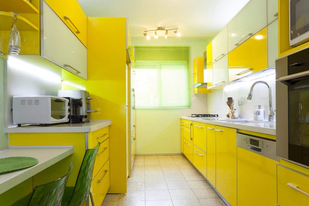华丽的厨房，白色和动态的黄色橱柜，以及安装在标准天花板上的轨道灯。