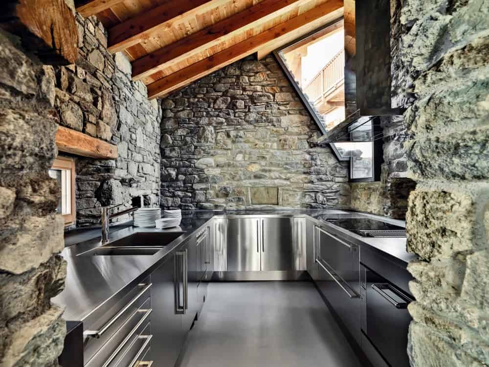 这间厨房很时髦，有石墙和带横梁的木质屋顶。不锈钢的设备和灰色的地板完美地结合在一起。