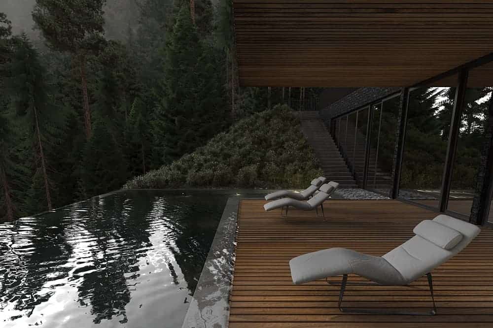 这是从泳池边的木地板上看到的景色，泳池边有舒适的草坪椅，面对着游泳池和远处的森林景观。