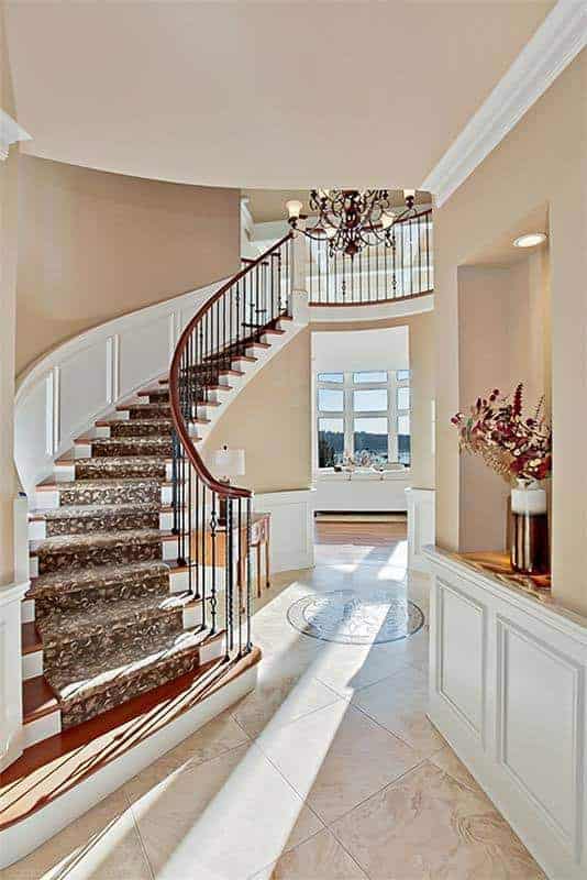 这个门厅设有一个优雅的弯曲楼梯，一个令人惊叹的吊灯悬挂在大理石瓷砖地板上。