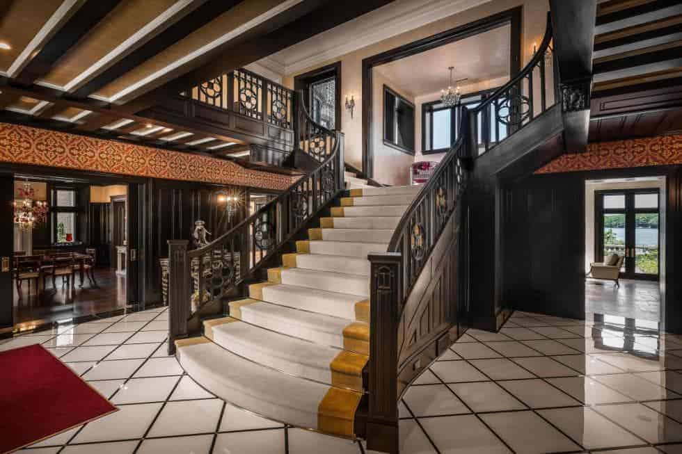 这是豪宅的门厅，正对着巨大的楼梯，楼梯上有昏暗的木栏杆和时髦的铁栏杆，与地板的白色瓷砖形成对比。