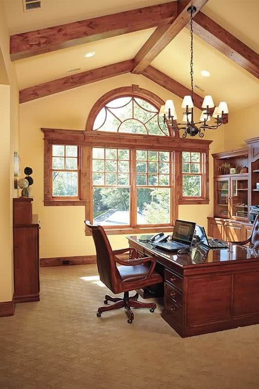 这个家庭办公室有一个高拱形天花板，暴露的木梁和木制桌子搭配舒适的座椅。