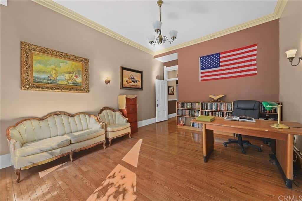 这个家庭办公室在硬木地板上有一张木桌和一把办公椅。它还有一个舒适的沙发和墙上的画。