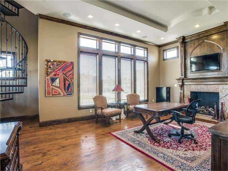 优雅的家庭办公室设有深色木桌，经典的红色地毯上有办公椅，壁炉与硬木地板相匹配。