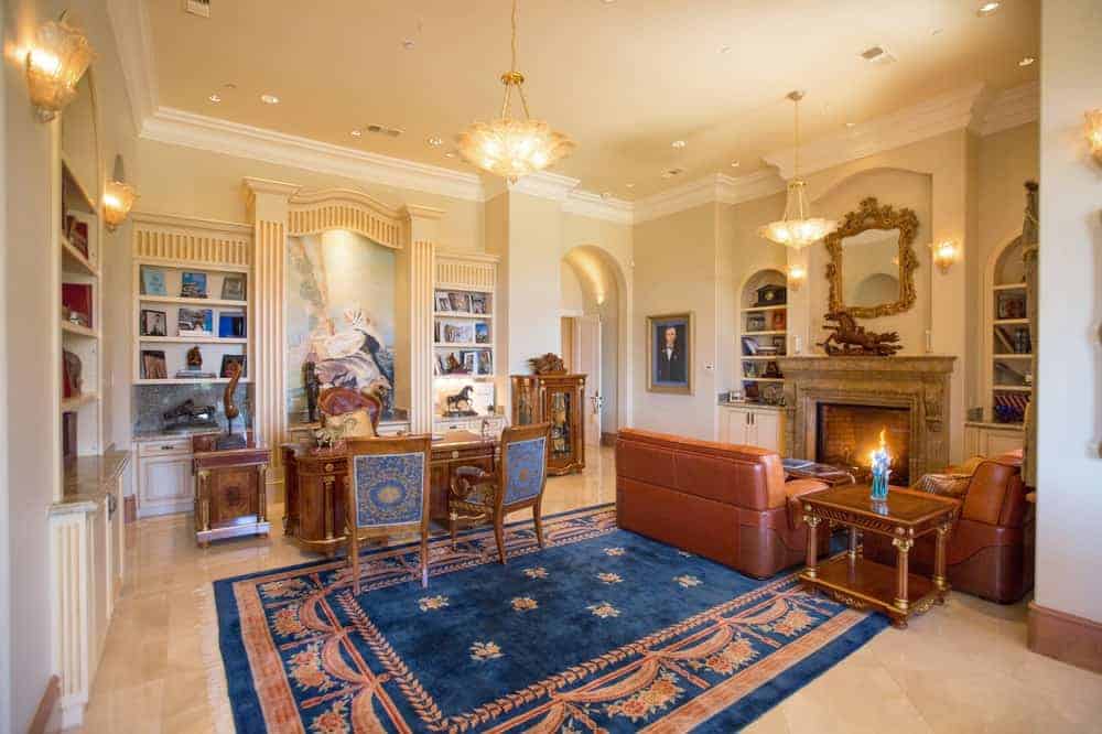 迷人的书房和家庭办公室的豪宅有一个古董木桌搭配漂亮的椅子。旁边是一张真皮沙发，面对着大壁炉，壁炉上方装饰着一面优雅的壁挂镜。