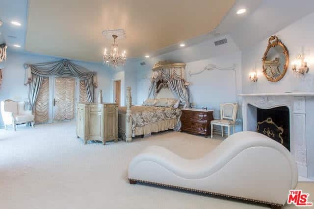 这间优雅的主卧室有一张可爱的床，由闪闪发光的吊灯照亮。屋内还有一座壁炉和一把舒适的白色椅子。