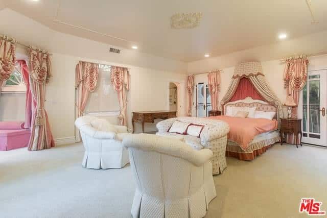 一个独特的女孩房间，有高高的拱形天花板和天花板灯。房间里还有一张时髦的粉色床和几把白色椅子。