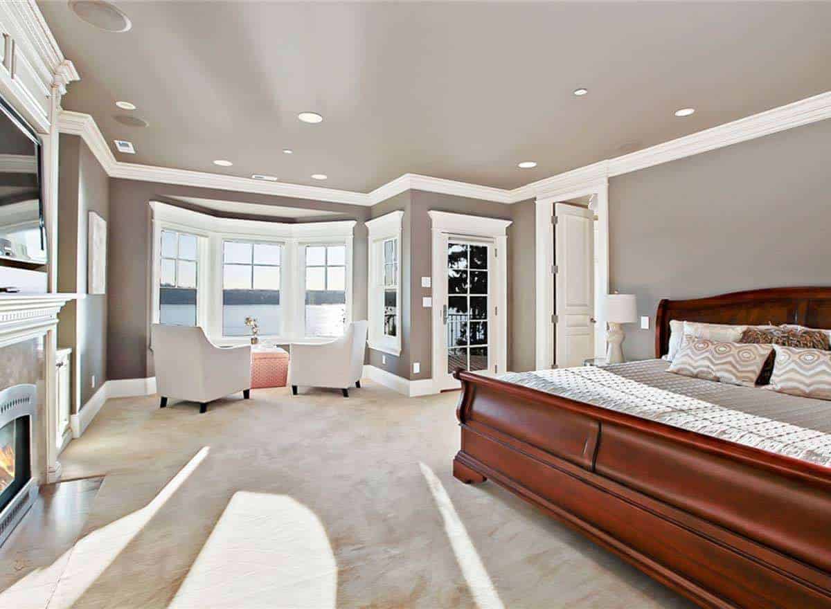这间主卧室有一张舒适的大床，铺着时尚的地毯地板。房子里还有一座壁炉，窗前还有一对白色椅子。