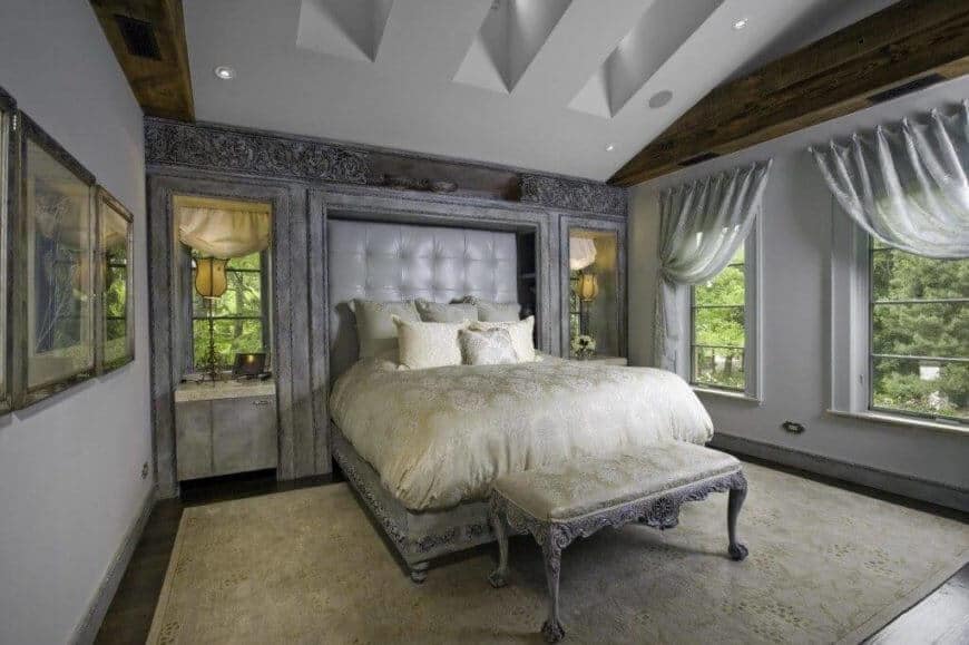 白色和灰色的卧室，嵌有人造皮革的纽扣簇床头板。床的框架是华丽的雕刻，与脚边的长凳和上面的内置装饰相匹配。