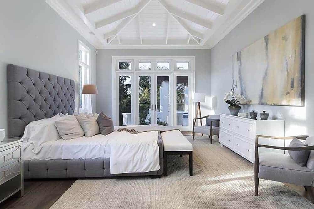 主卧室的特色是一张大床，顶部有灰色软垫床头板，高高的拱形天花板和裸露的横梁。