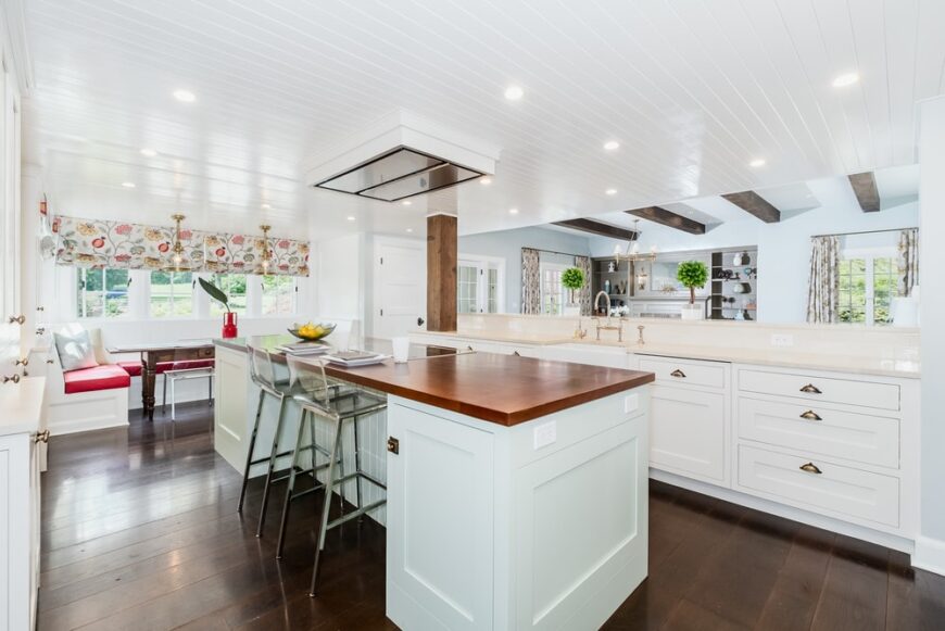 厨房里有明亮和白色的摇床橱柜和抽屉，辅以硬木地板和厨房岛台的木质台面。你可以看到在角落里有一根厚实的木柱连接着柜台和天花板。