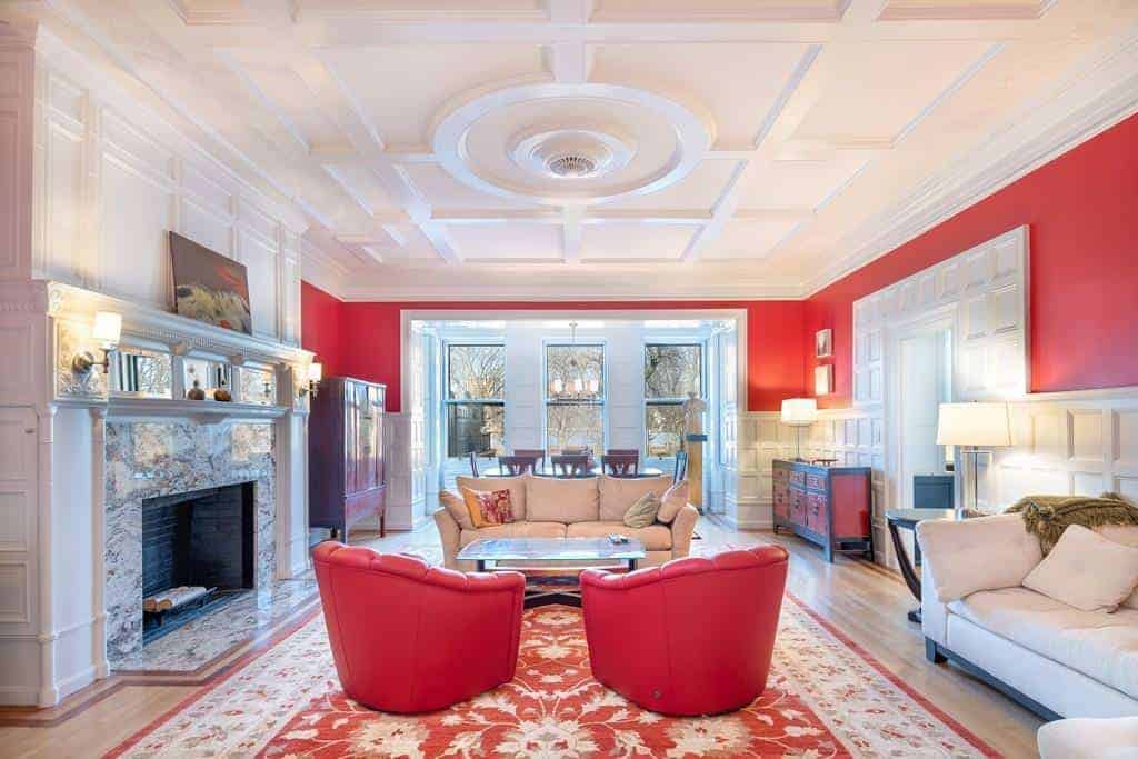这个宽敞的客厅以白色的墙壁为特色，带有一点红色，与红色华丽地毯上的红色沙发相匹配。
