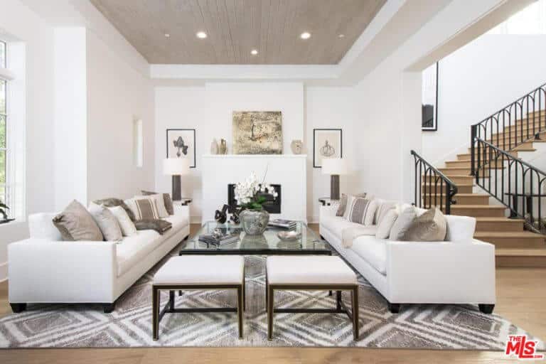 这个起居空间设有舒适的白色沙发和时尚地毯上的玻璃桌。它也有白色的墙壁，与硬木地板相匹配。