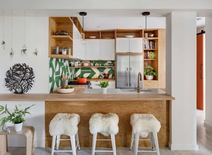 厨房的这一视图展示了l形的半岛，木制早餐吧台搭配白色凳子，与白色墙壁相匹配。这个半岛连接着一根厚厚的白色柱子，连接着地板和白色天花板。