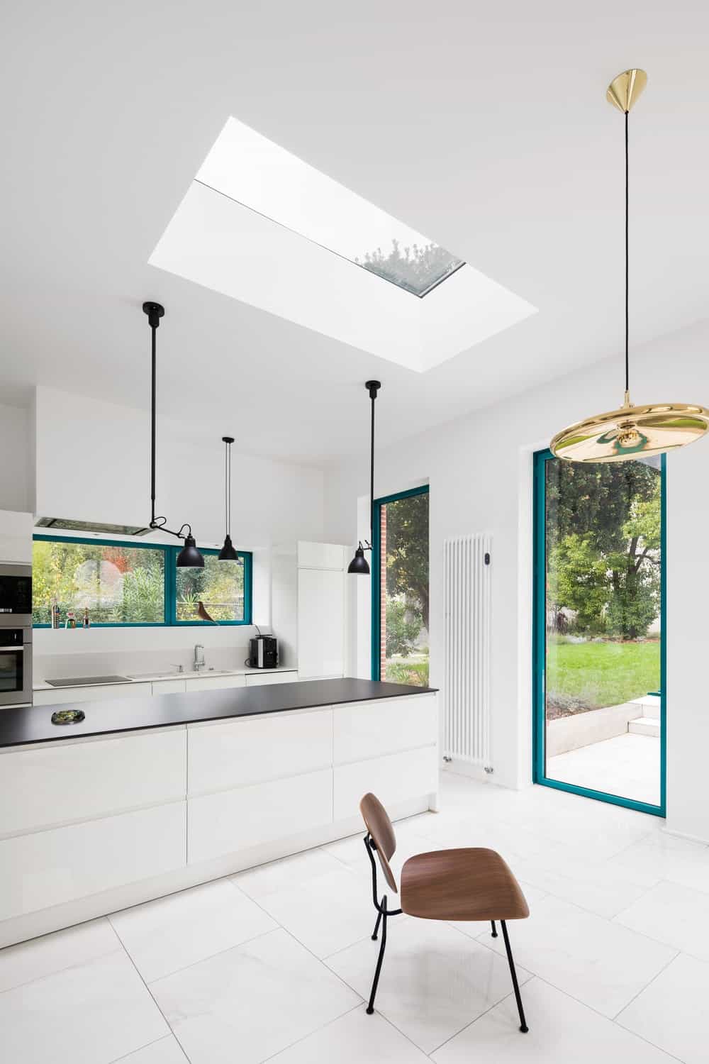 这是一个简单而辉煌的现代厨房，有狭长的设计。它有一个长长的白色厨房岛台，与带天窗的明亮天花板的黑色哑光台面形成对比。
