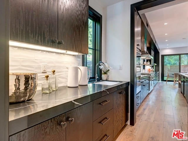 厨房的这一视图展示了它可爱的狭长设计，一排黑色橱柜衬墙，顶部是黑色大理石台面，与明亮的后挡板形成对比，由浮动橱柜照明。