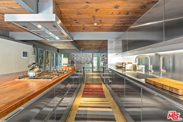 这是狭长的厨房，两侧都有现代化的不锈钢橱柜。这些与厨房岛台的木制台面和木制船板天花板搭配得很好，在烹饪区上方有一个现代的通风口。