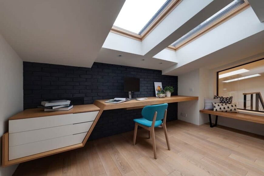 硬木地板与内置桌子的表面相匹配，桌子上有白色抽屉，与带有天窗的白色棚顶相匹配。这与书桌的黑色砖墙形成了鲜明的对比。