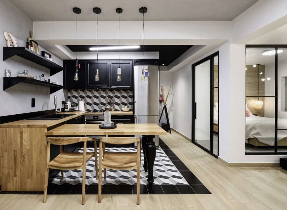 这个华丽的厨房有一个黑色和白色的托盘天花板，与地板的黑白图案瓷砖相匹配。这些延伸到后挡板。这与木质台面很好地配合，它延伸到边缘的内置桌子上，形成一个半岛。