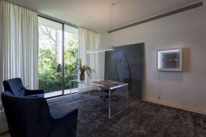 这是一个精致的现代住宅，有一张透明的桌子。这与黑色转椅后面的黑色地毯和黑色墙壁艺术品非常相配，在白色墙壁和天花板的映衬下显得非常突出。
