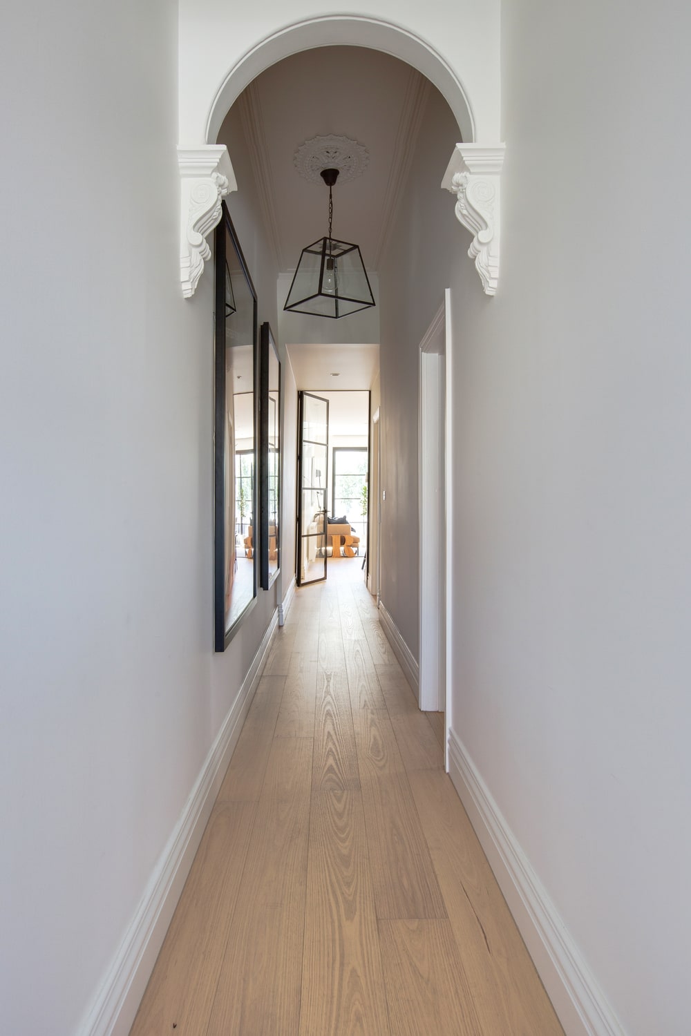 这是一个简单的走廊式门厅，白色的墙壁，白色的拱门和浅色的硬木地板，与黑色灯笼般的吊灯和壁挂式艺术品的框架形成对比。